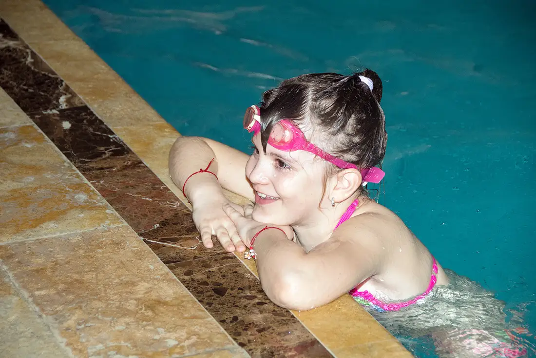 Fetiță zâmbind la marginea piscinei, după cursul de înot