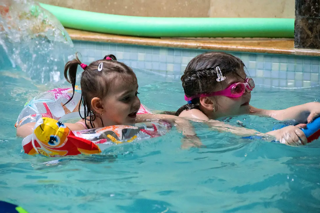 Două fetițe înotând împreună în piscina interioară